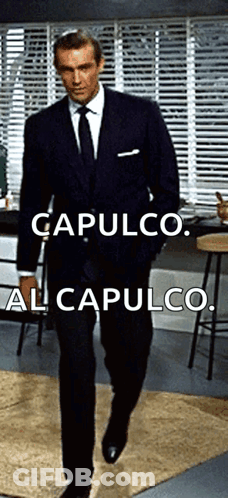 A Man In A Suit And Tie Is Walking In A Room With The Words Capulco Al Capulco Below Him GIF