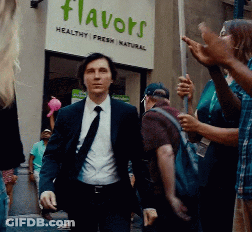 A Man In A Suit And Tie Is Walking In Front Of A Flavors Sign GIF