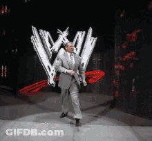A Man In A Suit And Tie Is Walking On A Stage In Front Of A W Logo GIF