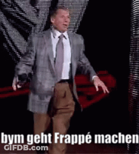 A Man In A Suit And Tie Is Walking On A Stage With The Words Bym Geht Frappe Machen On The Bottom . GIF