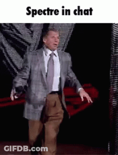 A Man In A Suit And Tie Is Walking On A Stage With The Words Spectre In Chat Below Him . GIF