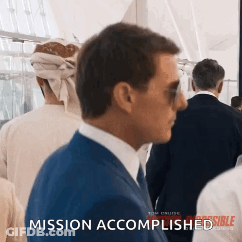 A Man In A Suit And Tie Is Walking Through A Crowd Of People And Says Mission Accomplished . GIF