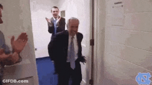 A Man In A Suit And Tie Is Walking Through A Doorway While Other Men Applaud . GIF