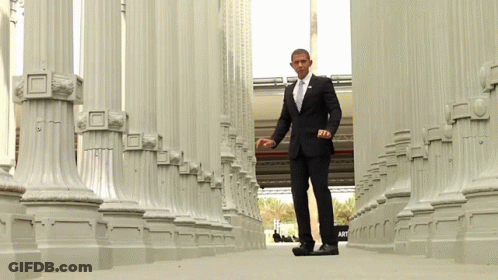 A Man In A Suit And Tie Is Walking Through Columns GIF