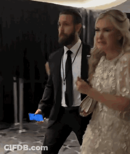 A Man In A Suit And Tie Is Walking With A Woman In A Dress GIF