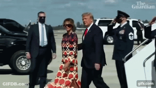 A Man In A Suit And Tie Is Walking With A Woman In A Dress .. GIF