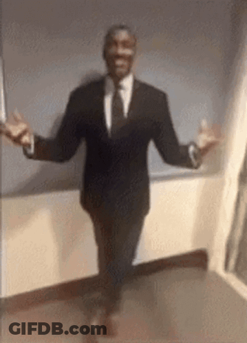 A Man In A Suit And Tie Is Walking With His Arms Outstretched . GIF