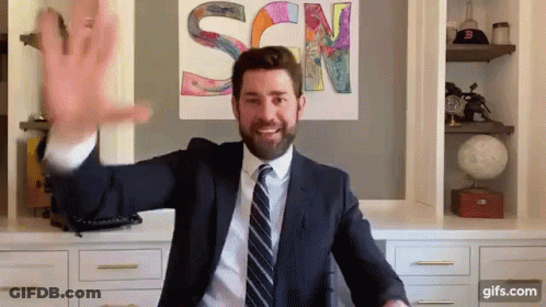 A Man In A Suit And Tie Is Waving His Hand In Front Of A Sign That Says Scn GIF