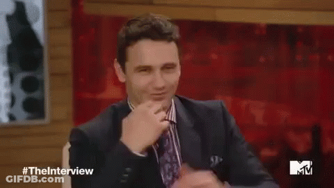 A Man In A Suit And Tie Is Waving His Hand While Sitting On A Stage . GIF