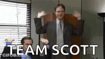 A Man In A Suit And Tie Is Waving His Hands In The Air In Front Of A Window . GIF