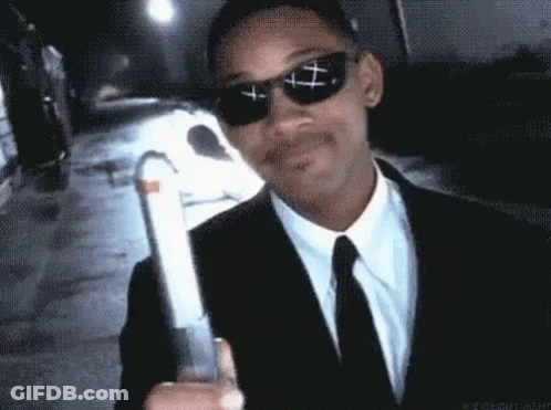 A Man In A Suit And Tie Is Wearing Sunglasses And Holding A Gun . GIF