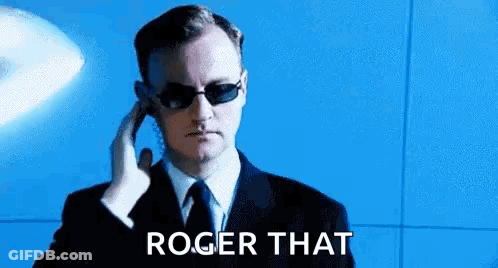 A Man In A Suit And Tie Is Wearing Sunglasses And Talking On A Phone . GIF