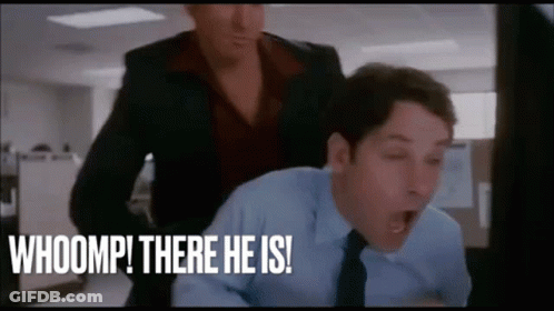 A Man In A Suit And Tie Is Yawning While A Woman Stands Behind Him And Says Whoomp There He Is ! GIF