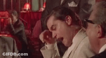 A Man In A Suit And Tie Is Yawning While Sitting At A Table In A Bar . GIF