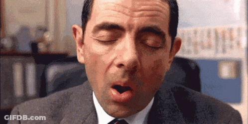 A Man In A Suit And Tie Is Yawning With His Mouth Open . GIF