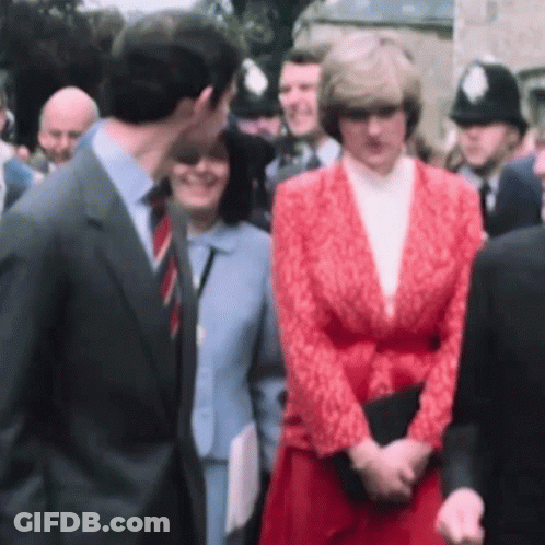 A Man In A Suit And Tie Kisses A Woman In A Red Jacket . GIF