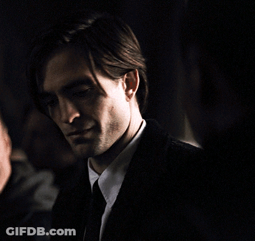 A Man In A Suit And Tie Looks At The Camera In A Dark Room GIF