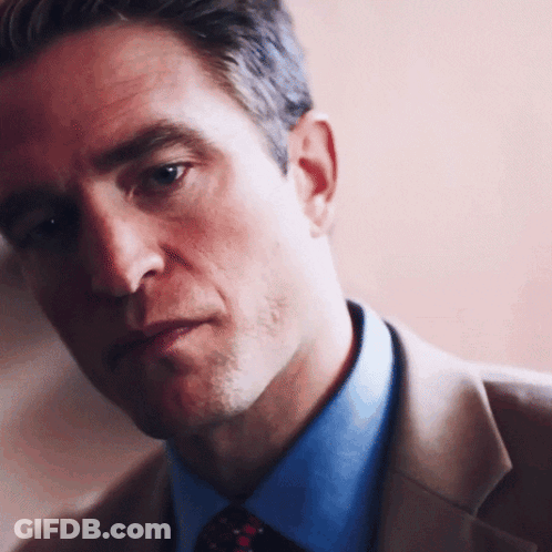 A Man In A Suit And Tie Looks At The Camera With A Serious Look On His Face GIF