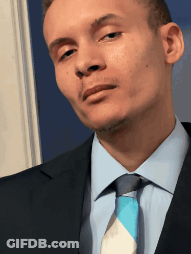 A Man In A Suit And Tie Looks At The Camera With His Eyes Closed GIF