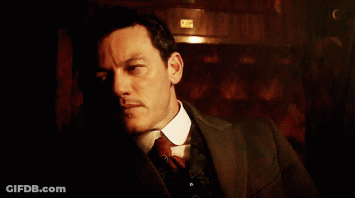 A Man In A Suit And Tie Looks Down At Something GIF