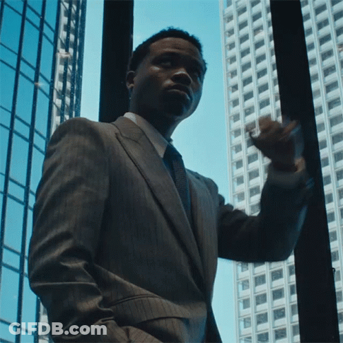 A Man In A Suit And Tie Looks Out A Window GIF