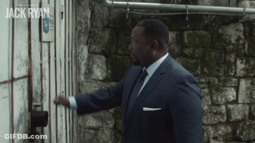 A Man In A Suit And Tie Opens A Door With The Name Jack Ryan On The Wall Behind Him GIF
