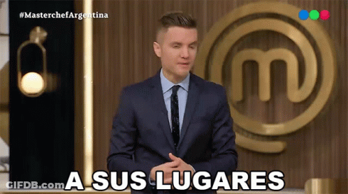 A Man In A Suit And Tie Says A Sus Lugares In Front Of A Masterchef Logo GIF