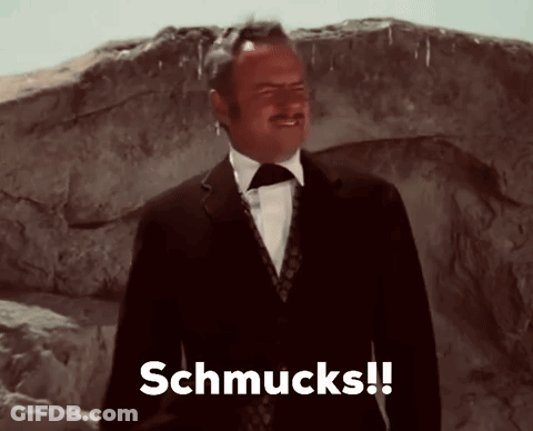 A Man In A Suit And Tie Says Schmucks In Front Of A Rock GIF