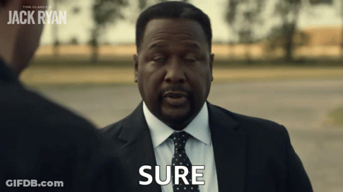 A Man In A Suit And Tie Says Sure In Front Of A Sign That Says Jack Ryan GIF