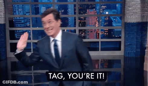 A Man In A Suit And Tie Says Tag You 'Re It In Front Of A Window GIF