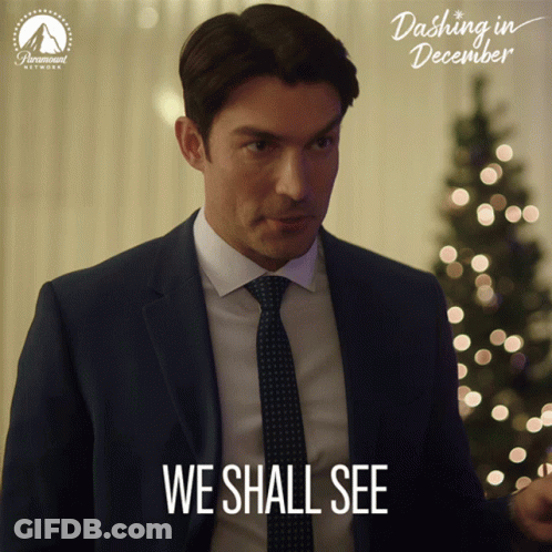 A Man In A Suit And Tie Says " We Shall See " In Front Of A Christmas Tree GIF