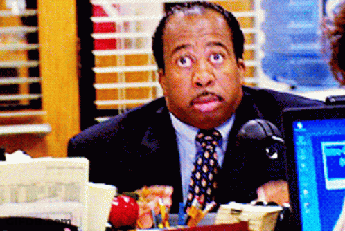 A Man In A Suit And Tie Sits At A Desk In Front Of A Computer GIF