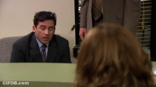 A Man In A Suit And Tie Sits At A Desk In Front Of A Woman GIF