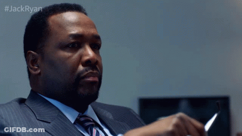 A Man In A Suit And Tie Sits At A Desk With The Hashtag #Jackryan On The Bottom GIF