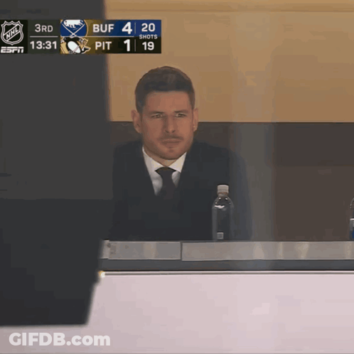 A Man In A Suit And Tie Sits In A Broadcast Booth With A Bottle Of Water GIF