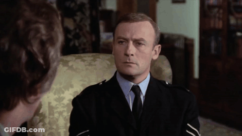A Man In A Suit And Tie Sits In A Chair GIF