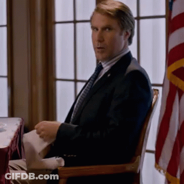 A Man In A Suit And Tie Sits In A Chair GIF