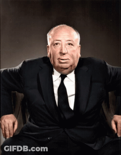 A Man In A Suit And Tie Sits In A Chair With His Hands On His Knees GIF