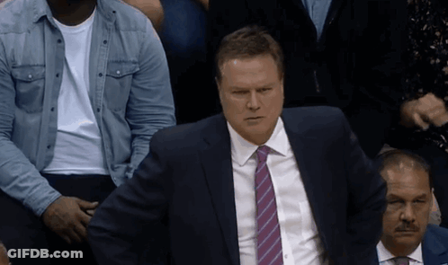 A Man In A Suit And Tie Sits In A Crowd Of People GIF