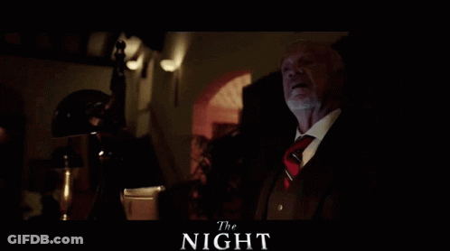 A Man In A Suit And Tie Sits In A Dark Room With The Words The Night Written Above Him GIF