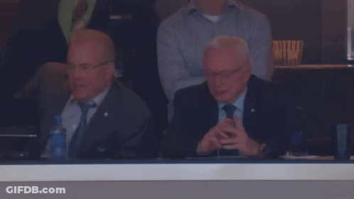 A Man In A Suit And Tie Sits In A Stadium Watching A Game GIF