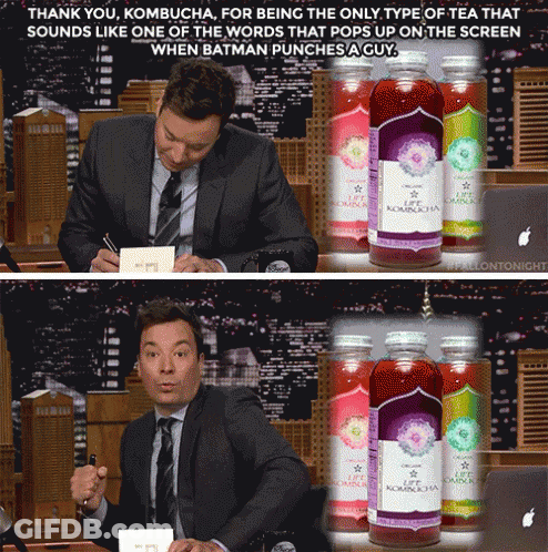 A Man In A Suit And Tie Sits In Front Of A Bottle Of Kombucha GIF