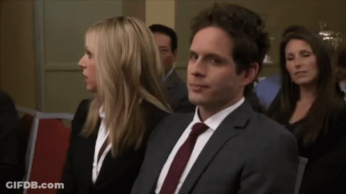 A Man In A Suit And Tie Sits Next To A Woman In A Black Suit GIF