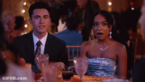 A Man In A Suit And Tie Sits Next To A Woman In A Strapless Blue Dress GIF