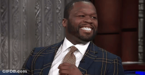 A Man In A Suit And Tie Sits On A Blue Couch GIF
