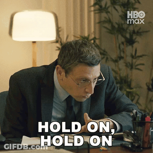 A Man In A Suit And Tie Sitting At A Desk With The Words Hold On Hold On GIF