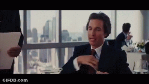 A Man In A Suit And Tie Sitting At A Table GIF