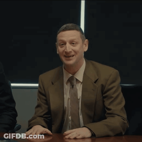 A Man In A Suit And Tie Sitting At A Table With The Word Coward Written On His Face GIF