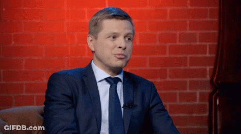 A Man In A Suit And Tie Sitting In Front Of A Brick Wall GIF