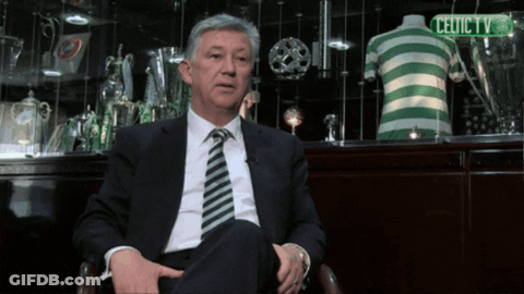 A Man In A Suit And Tie Sitting In Front Of A Celtic Tv Sign GIF